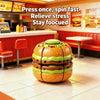 An orange hamburger-shaped fidget ball is shown on a tiled floor in a fast food restaurant setting.