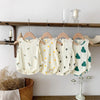 A set of cream and green baby cotton sleeveless jumpsuit bodysuits hanging on a wooden shelf.