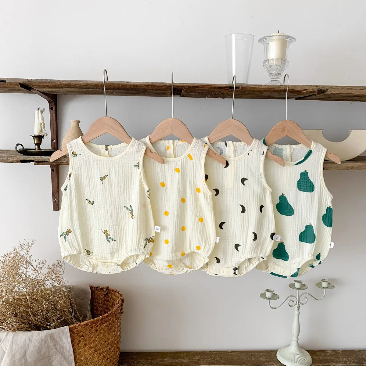 A set of cream and green baby cotton sleeveless jumpsuit bodysuits hanging on a wooden shelf.