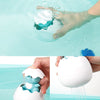 A hand dips a white bath toy shaped like a duck or penguin into clear water, creating a spray of water.
