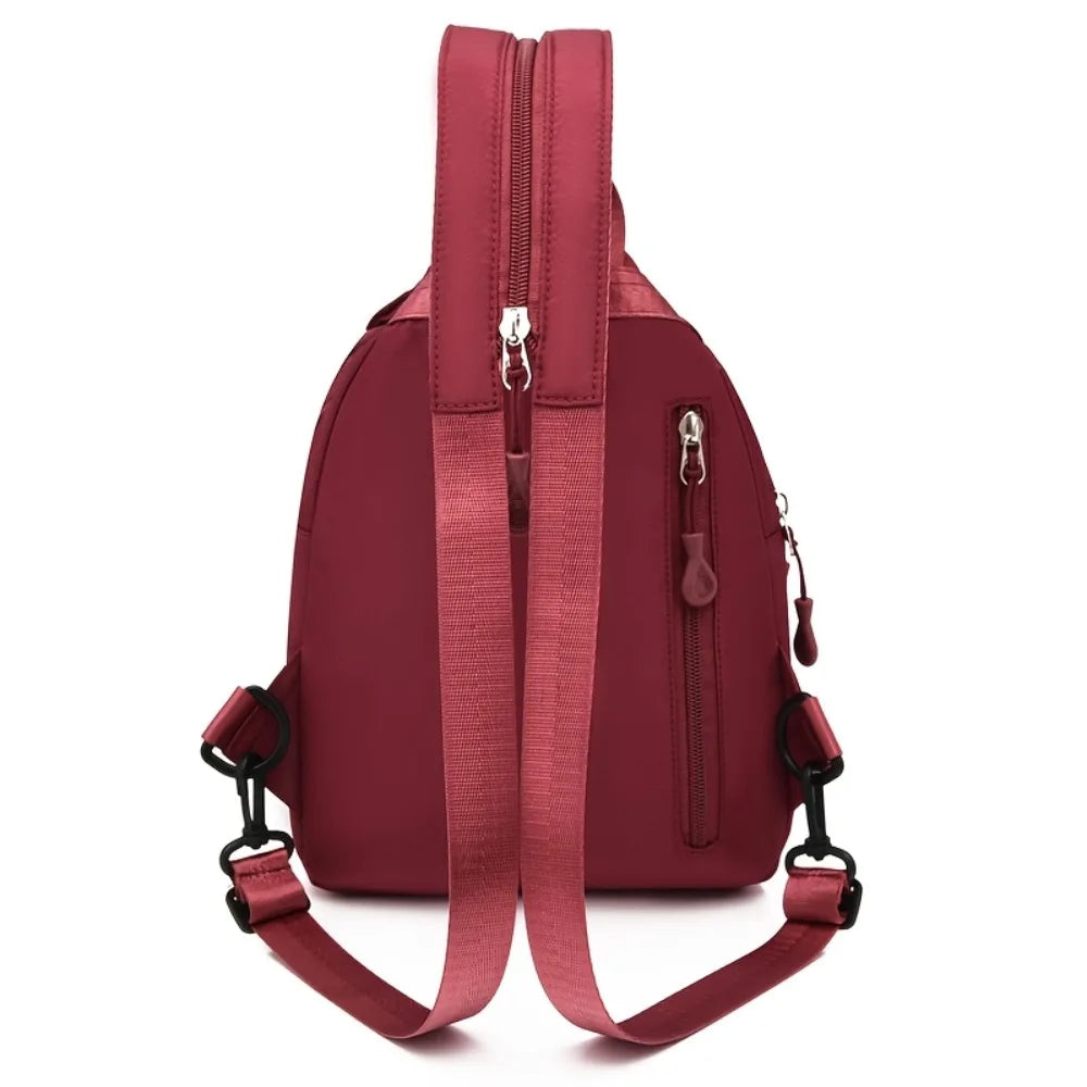 A maroon mini backpack with a zipper closure and adjustable strap is shown against a white background.