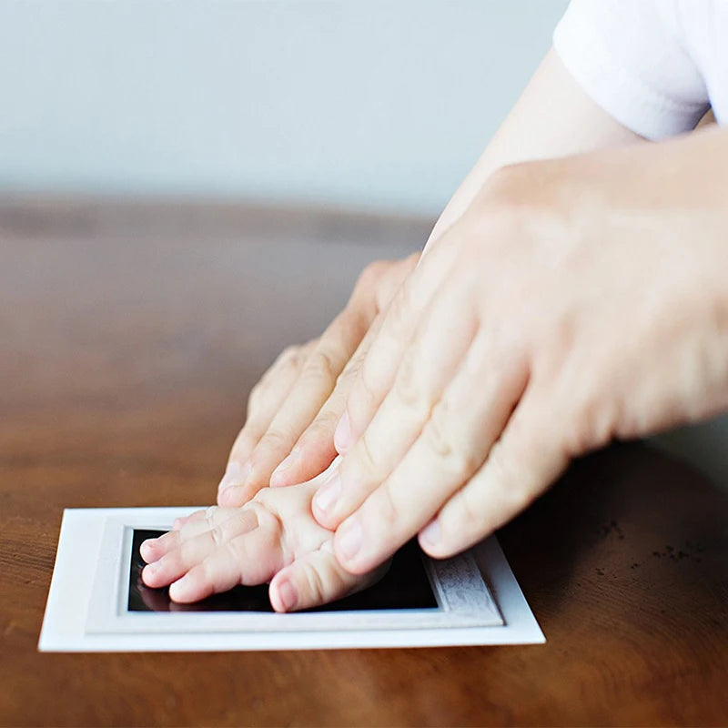 A hand is pressing a baby's handprint into an inkless keepsake plate on a wooden surface.