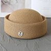 A beige straw pillbox sun hat with a wide brim resting on a gray surface.