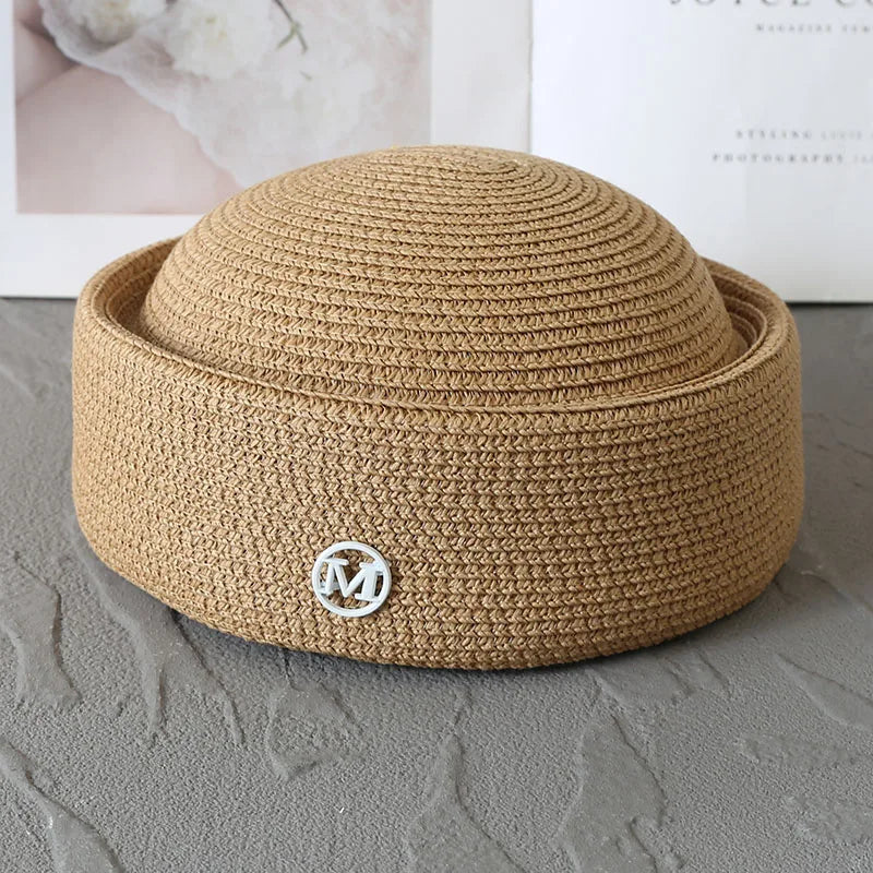 A beige straw pillbox sun hat with a wide brim resting on a gray surface.