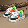 A pair of kids' breathable casual sneakers featuring white, orange, and teal accents with a green lining, resting on a brown 