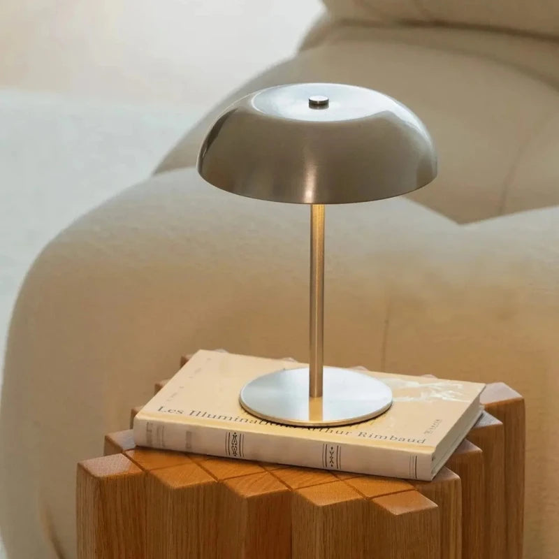 A silver portable touch table lamp with a gold-toned stand rests on a stack of books.