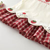 A cream summer pinafore dress featuring a red plaid ruffle and strawberry and bunny print details.