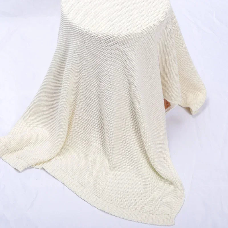 A cream-colored baby knit cotton blanket with a loose, wrap style is shown.