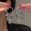 A pair of silver gold geometric tassel drop earrings being held by a person's fingers.