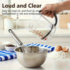 A hand holds a clear measuring cup with red embossed markings, positioned above a metal bowl and whisk.