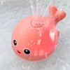 A pink musical whale bath toy is spraying water in a clear bath.