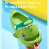 A green kids clog sandal with a happy tooth design is held by a hand.