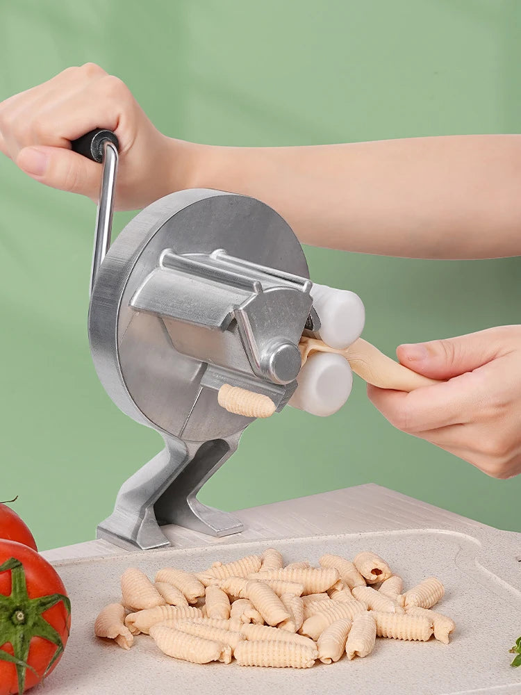 A hand is using a Cavatelli maker machine to roll out fresh pasta strands onto a cutting board.