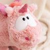 A close-up of a pink unicorn plush toy with pink accents and large white eyes.