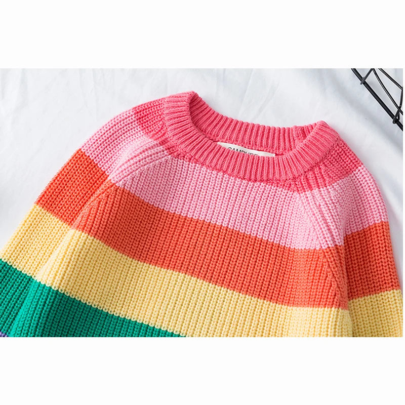 A close-up of a girls' rainbow striped knit sweater featuring horizontal bands of pink, orange, yellow, and green.