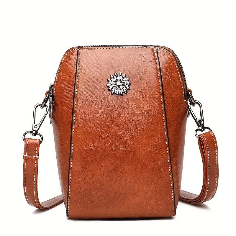 Brun skinncrossbody-telefonveske med dekorativt metallblomst-emblem og justerbar stropp.