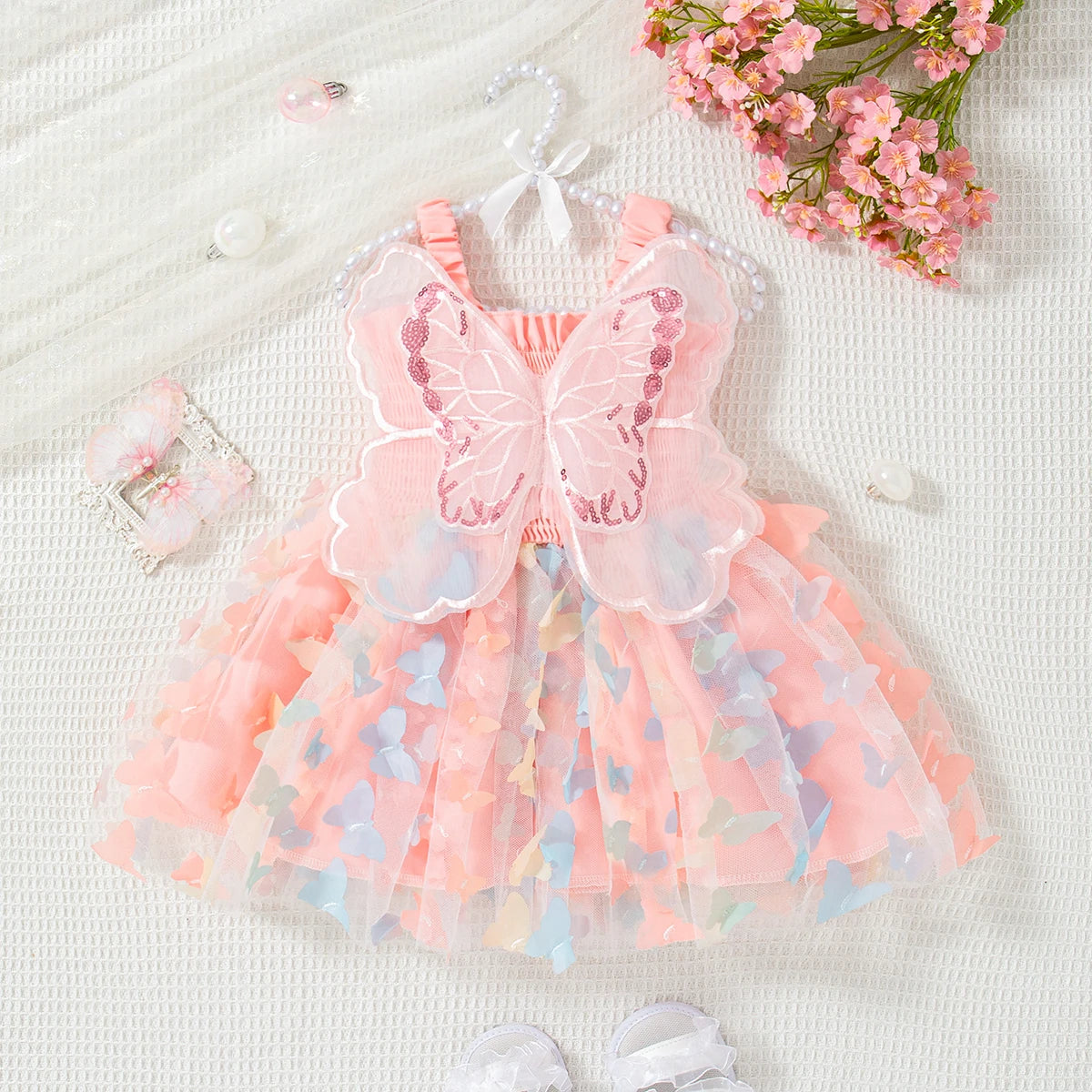 A pink butterfly tulle dress for a baby girl displayed on a white surface with pink flowers and beads.
