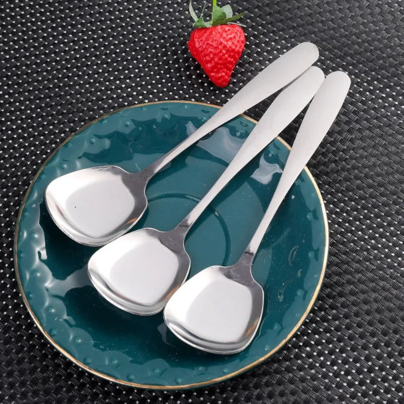 A set of three stainless steel serving spoons resting on a teal plate with a strawberry garnish.