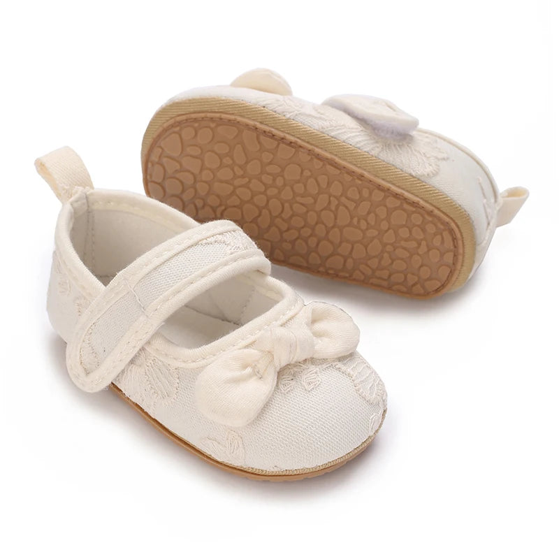A pair of soft non-slip baby first walker shoes in cream color with a textured sole.