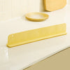 Protector de salpicaduras adhesivo amarillo con patrón zigzag sobre encimera blanca junto a platos apilados.