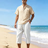 A man wearing light beige linen drawstring capri pants standing on a sandy beach near the ocean.