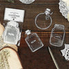 A set of three clear glass bottle bookmarks with labels on a dark wooden surface.