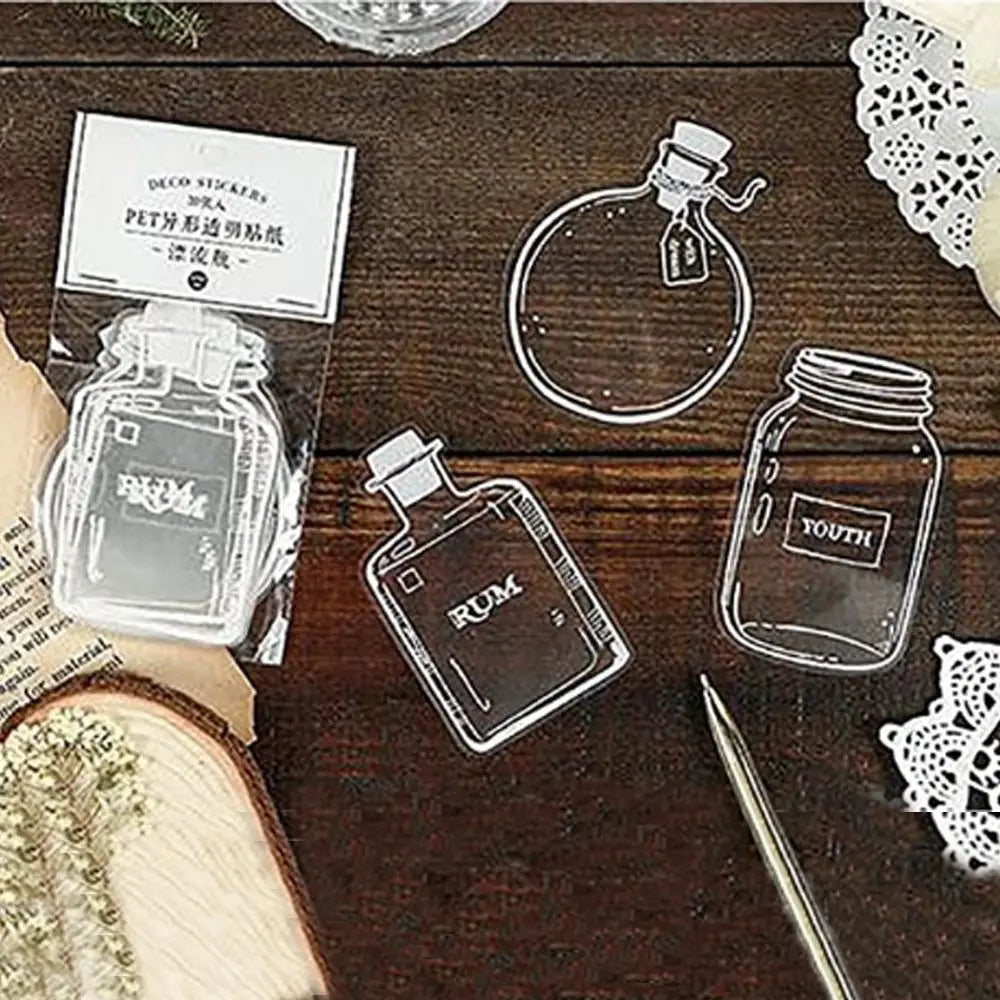 A set of three clear glass bottle bookmarks with labels on a dark wooden surface.