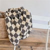 A pair of kids' washed cotton harem pants with a black and beige checkered pattern folded on a white wooden chair.