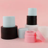 A stack of refillable travel face cream jars in black and white shades on a pink background.