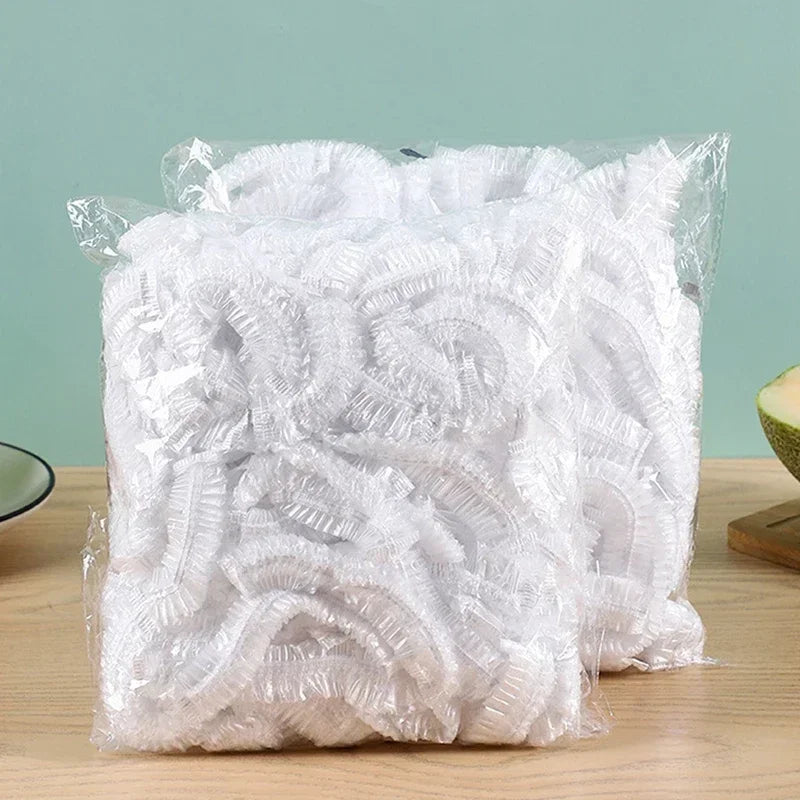 A clear plastic bag filled with a large quantity of white disposable shower caps with elastic.