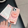 Soporte magnético para teléfono en forma de cerdito rosa 3D, descansando sobre una superficie negra junto a una publicación d