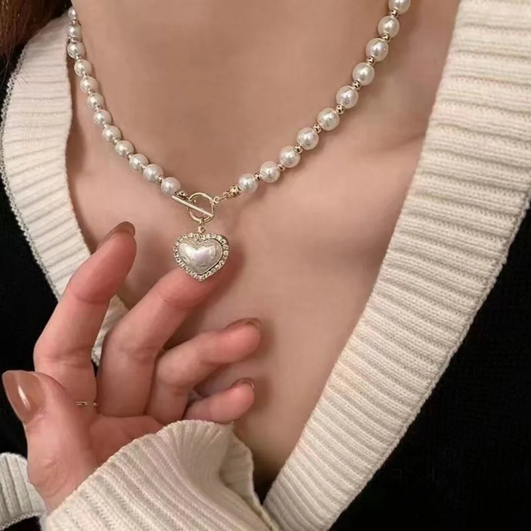 A close-up of an elegant necklace featuring a heart pendant made with simulated pearls, worn against a light sweater.