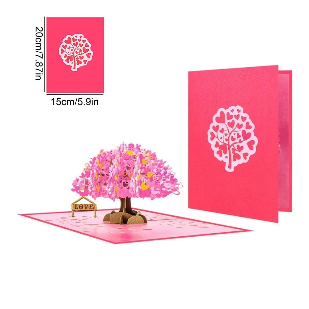 A pink pop-up card featuring a white silhouette of a love tree on the cover and a pink floral tree design.