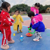 Three young children playing a colorful ring toss and stacking cups game outdoors on a blue mat.