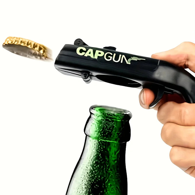 A hand holds a black cap gun style bottle opener, with a metal ring visible, next to a green glass bottle.