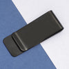 A black classic metal tie clip resting on a blue-gray surface.