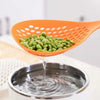 An orange long-handled kitchen strainer spoon is pouring green peas into a metal bowl.