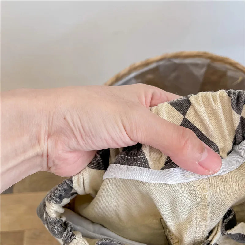 A hand is holding up kids' washed cotton harem pants with pockets, showing the fabric and stitching.