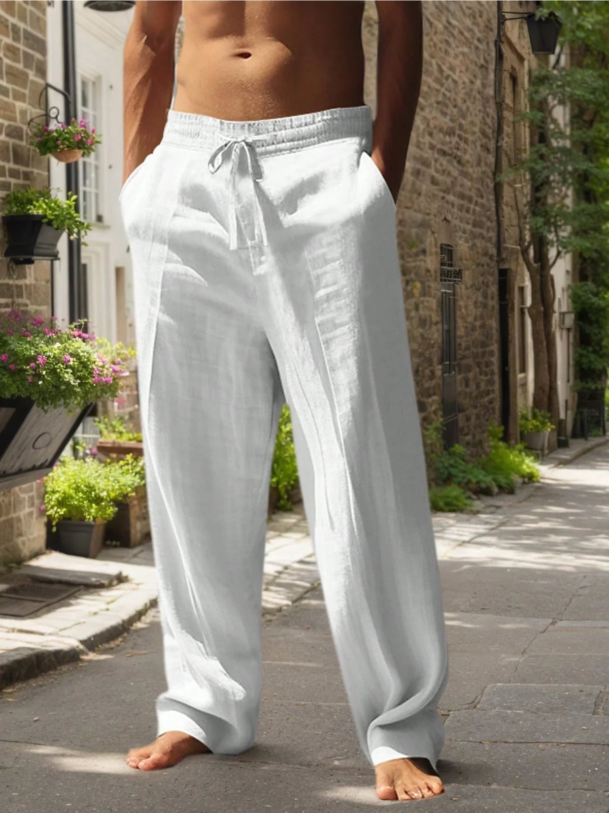 Hombre con pantalones casuales blancos de corte holgado parado al aire libre en una acera de piedra.