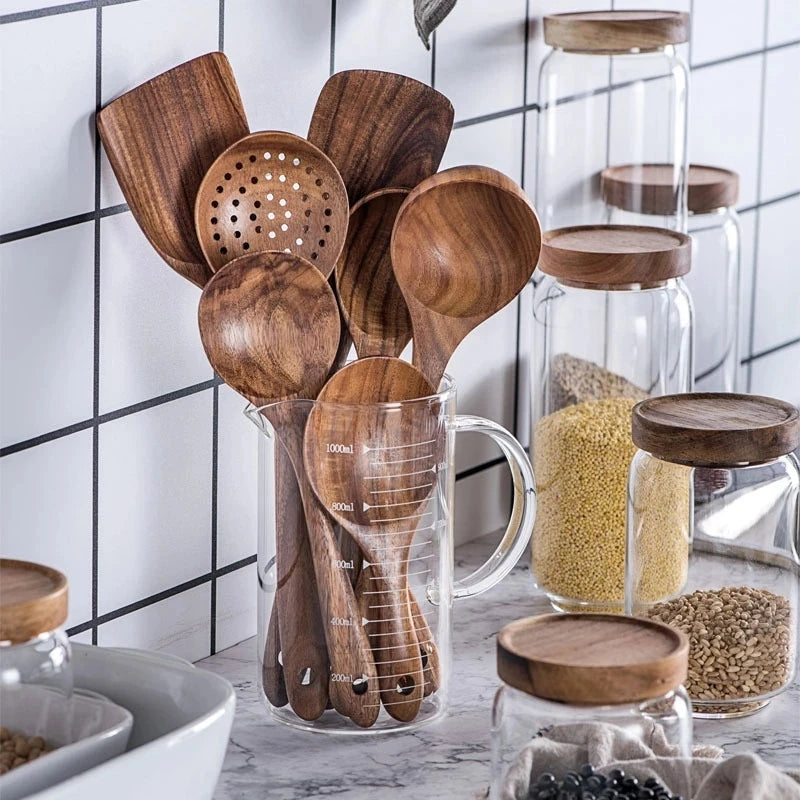 A collection of natural teak wood cooking utensils, including spatulas and spoons, displayed in glass jars.