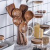 A collection of natural teak wood cooking utensils, including spatulas and spoons, displayed in glass jars.