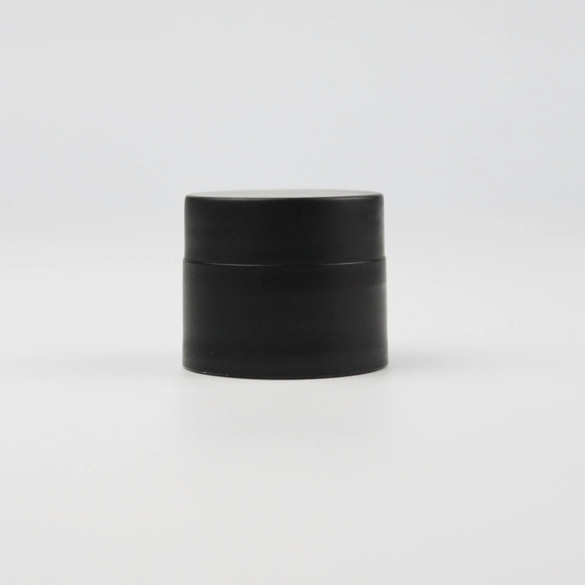 A black jar of refillable travel face cream with a leak-proof lid.
