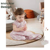 A toddler is sitting on the floor wearing a pink cotton baby sleeping sack with a two-way zipper.