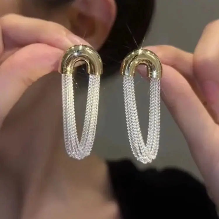 Pair of gold geometric tassel drop earrings being held by a person.