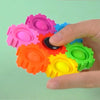 A hand is holding and manipulating a colorful set of pink, blue, orange, and green plastic gears or building blocks.