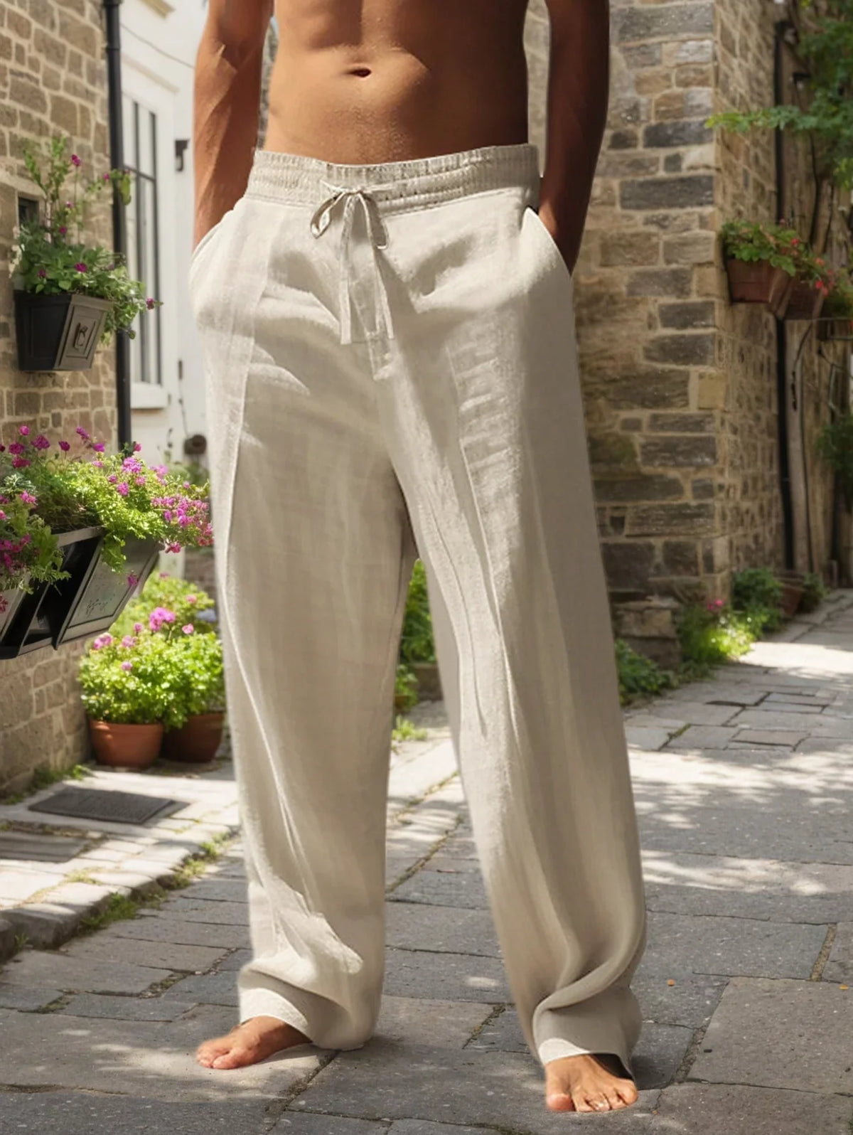 Hombre con pantalones casuales beige claro y holgados, atados a la cintura, de pie en un camino de piedra al aire libre.