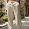 Hombre con pantalones casuales beige claro de ajuste holgado atados en la cintura, de pie sobre un camino de piedra.