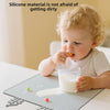 A baby is eating from a glass on a silicone feeding placemat with teething edges.