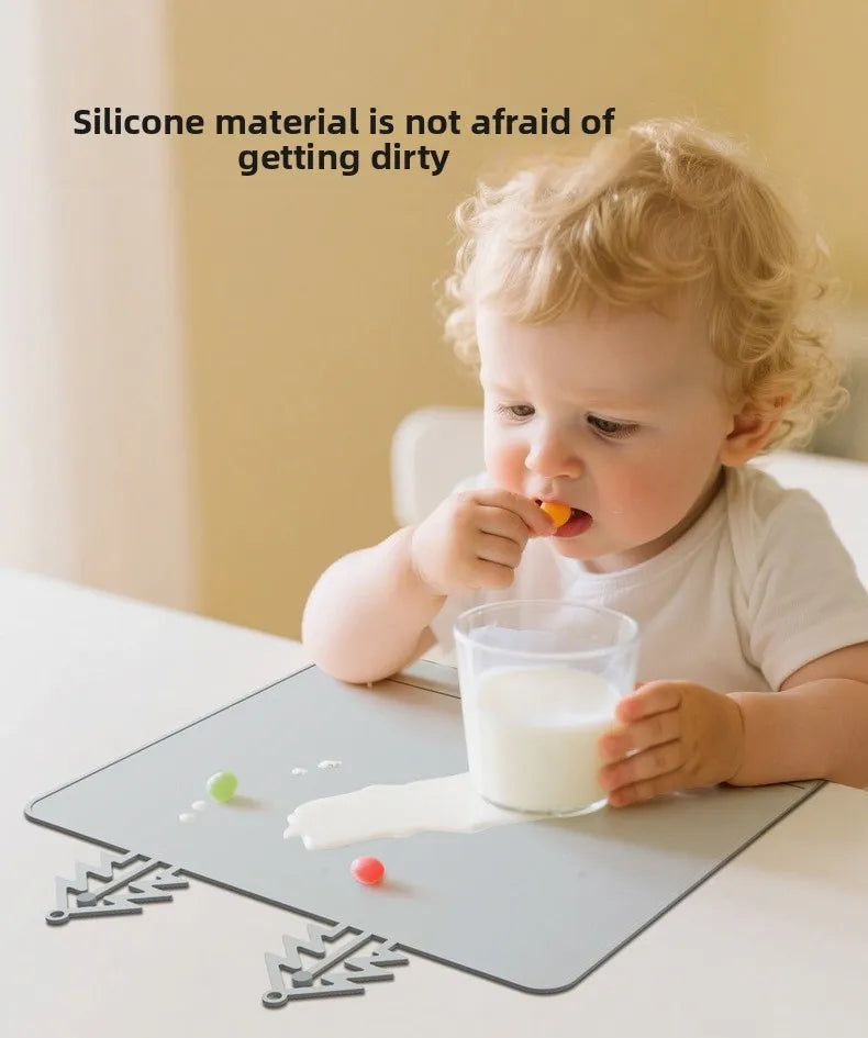 A baby is eating from a glass on a silicone feeding placemat with teething edges.