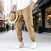 A man wearing tan cargo pants and a white shirt walks outdoors while holding a straw hat.